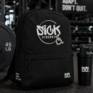 May include: Black backpack and shaker bottle set. The backpack features the text "Sick Strength" in a white circular design, with a wheelchair symbol. The shaker bottle has the same logo. The background includes gym equipment and the text "Discipline, Adapt, Don't Quit."