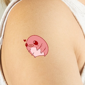 May include: A pink cartoon tardigrade with a red heart above its head. The tardigrade is on a person's arm.