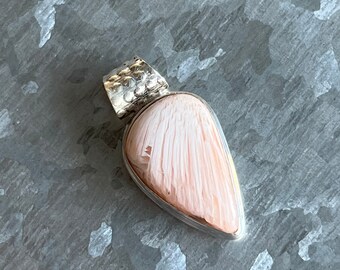 Op de afbeelding: Een traanvormige hanger met een roze en witte schelpcabochon, gezet in sterling zilver.