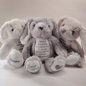 May include: Three soft toy bunny rabbits in white, grey, and light grey. The central bunny has the text "Here's a special hug between us two. So you are always with me and I am always with you." The left bunny has "Mommy" on its foot, and the center bunny has "Best Friend".