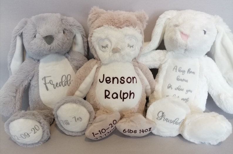 May include: Three plush stuffed animals, a gray bunny, a tan owl, and a white bunny. The gray bunny is embroidered with the name "Fredd", the date "12-09-20", and the weight "1-7oz". The tan owl is embroidered with the name "Jenson Ralph", the date "1-10-20", and the weight "6lbs 14oz". The white bunny is embroidered with the text "A hug from heaven for when you need it most" and the word "Grandad".