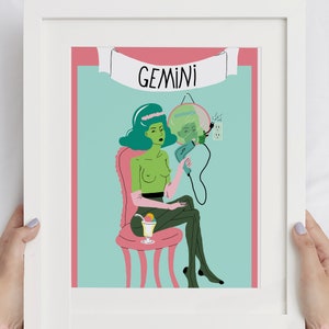 May include: A framed art print with a quirky illustration of the Gemini zodiac sign. The artwork shows a green-skinned figure on a pink chair, holding a mirror and a hairdryer. The word "GEMINI" is displayed above the figure in a banner.