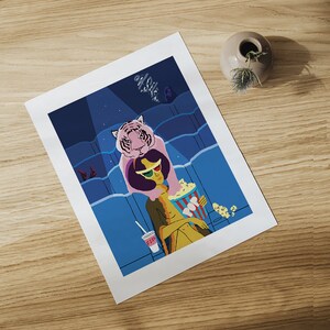 May include: A print depicting a movie theater scene with a person wearing 3D glasses and holding popcorn. A pink tiger is draped over the person's shoulders. A drink with the text "Fiz" is in the image. The background is blue.