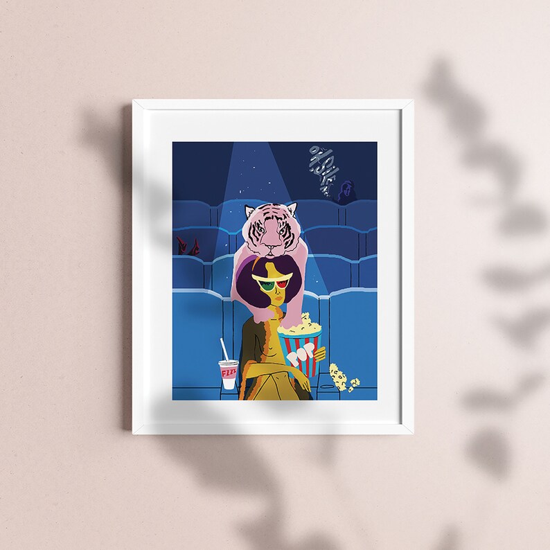 May include: A framed art print featuring a whimsical illustration of a person in 3D glasses at a movie theater, with a pink tiger above them. A popcorn bucket and drink are in the foreground. The background shows theater seating.