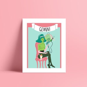 May include: A framed art print with a quirky illustration of a green-skinned figure seated on a pink chair, holding a mirror. The word "GEMINI" is displayed on a banner above. The background is light blue and pink.