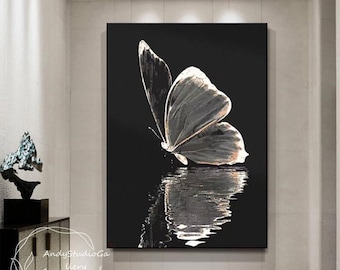 May include: A black and white painting of a butterfly with its wings spread out, reflecting in a body of water. The butterfly is in the upper right corner of the painting, and the water is in the lower left corner. The painting is framed in a black frame.
