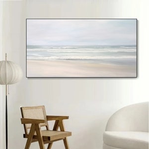 May include: A framed painting of a seascape with a white sandy beach and blue ocean waves. The painting is in a minimalist style with soft colors and a calming atmosphere.