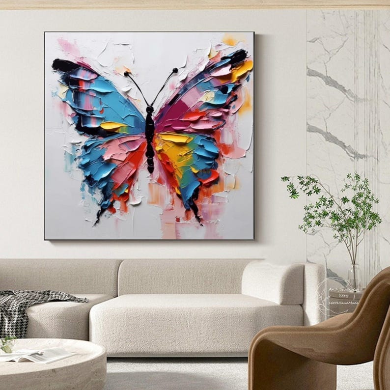 May include: A vibrant, textured butterfly painting with a white background. The butterfly features wings in shades of blue, pink, yellow, and orange, with black antennae and body. The artwork is displayed in a black frame.