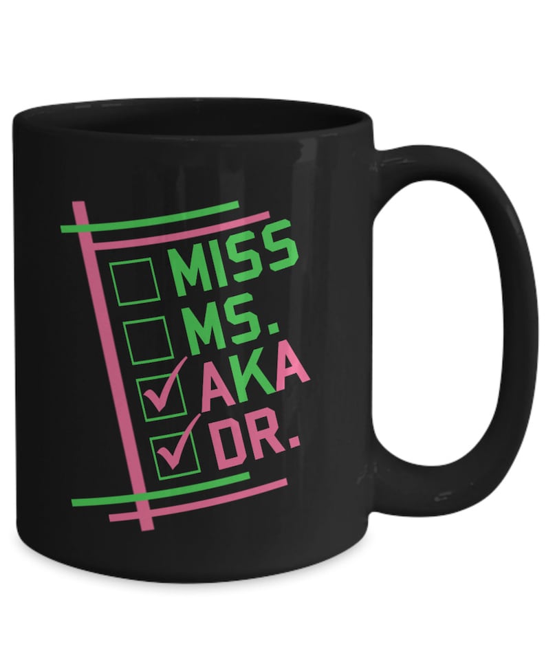 Puede incluir: Taza de cer&aacute;mica negra con las palabras "MISS MS. AKA DR." en verde y rosa. La taza presenta casillas de verificaci&oacute;n junto a "AKA" y "DR.". La taza tiene un asa curva.