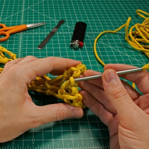 May include: A person's hands are shown working on a yellow paracord project. The person is using a needle to weave the paracord together. The project is being worked on a green cutting mat.