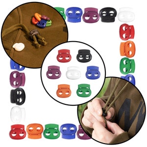 May include: Assortment of colorful plastic toggle clasps for cords and drawstrings. The toggles are in various colors, including red, orange, yellow, green, blue, purple, black, and white. The toggles are shown in a close-up view and in a larger view on a hoodie.