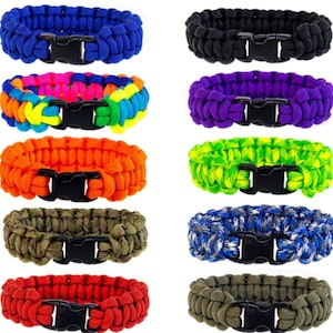 Könnte beinhalten: Zehn bunte Paracord-Armbänder mit schwarzen Kunststoffschnallen. Die Armbänder sind aus gewebtem Paracord gefertigt und in verschiedenen Farben erhältlich, darunter Blau, Lila, Grün, Orange, Rot und Tarnmuster.