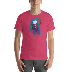 May include: A pink heather t-shirt with a graphic of a female superhero in a black and white suit with a white mask. The superhero is in a dynamic pose with a colorful background.