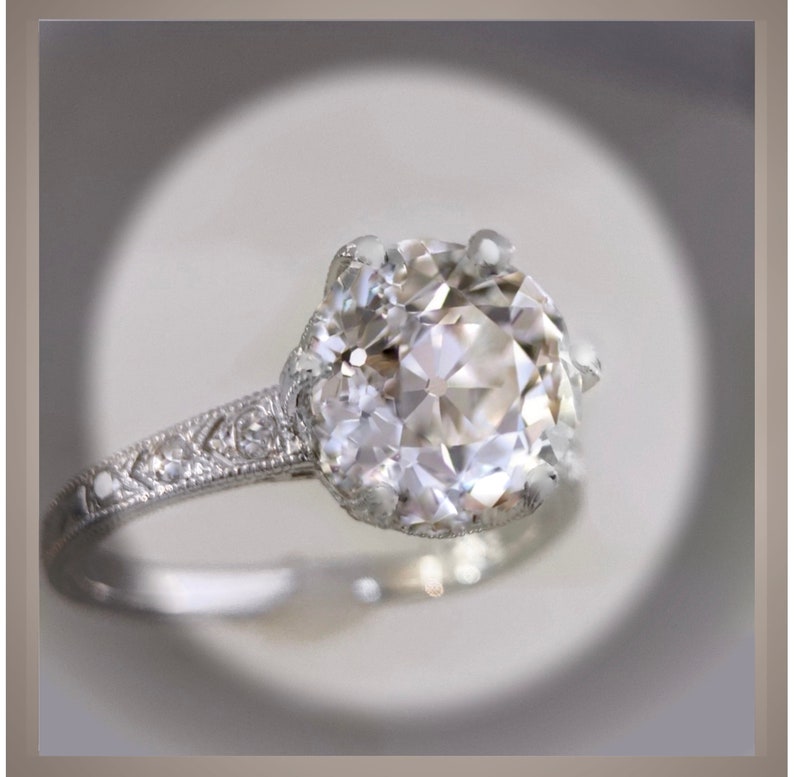 May include: A silver engagement ring with a large, round, clear diamond set in a delicate, ornate setting. The band is adorned with smaller diamonds.