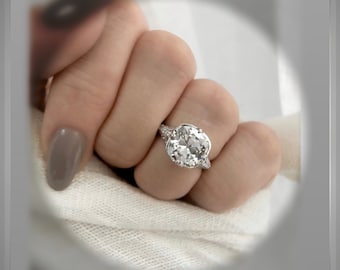 May include: A close-up of a hand wearing a silver ring with a large, round, clear gemstone. The ring has a delicate, intricate design.