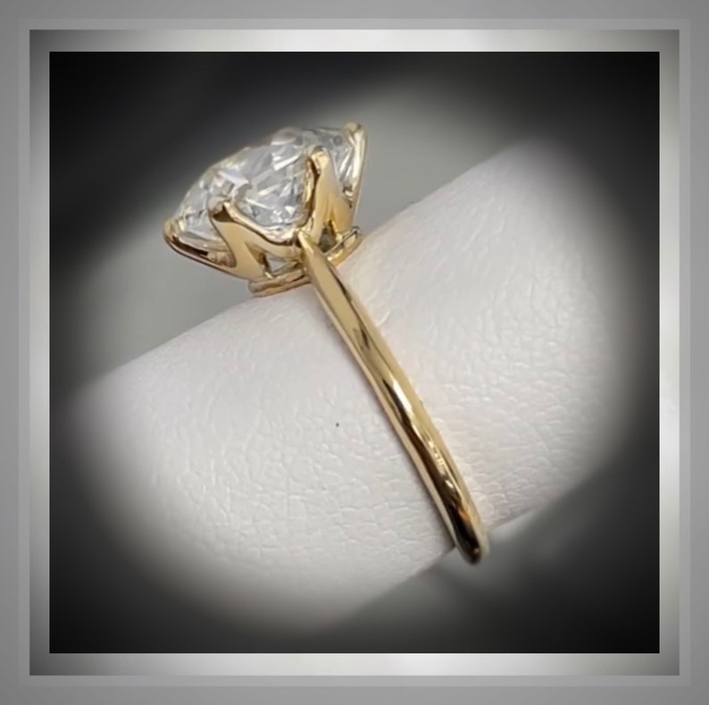 May include: A gold engagement ring with a large, clear, round diamond set in a prong setting. The ring is on a white background.