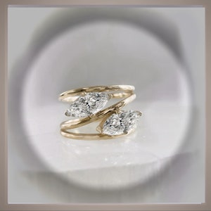 Könnte beinhalten: Ein goldener Ring mit zwei Marquise-Diamanten, die in einem verdrehten Band gefasst sind.