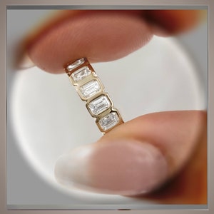 May include: A gold band ring with a row of emerald-cut diamonds.