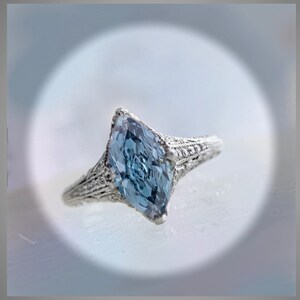 Pu&ograve; includere: Un anello d'argento con una pietra preziosa di forma marquise blu chiaro incastonata in un design a filigrana.