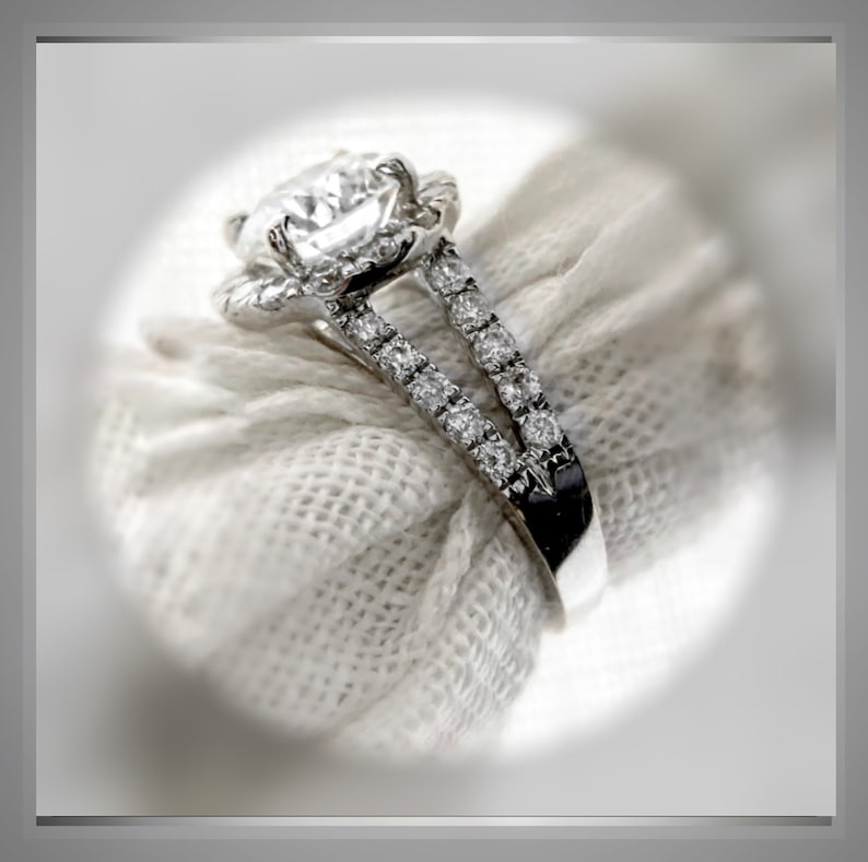 Op de afbeelding: Een diamanten verlovingsring met een halo-setting en een gesplitste band. De ring is gemaakt van witgoud en heeft een grote, ronde middelste steen.