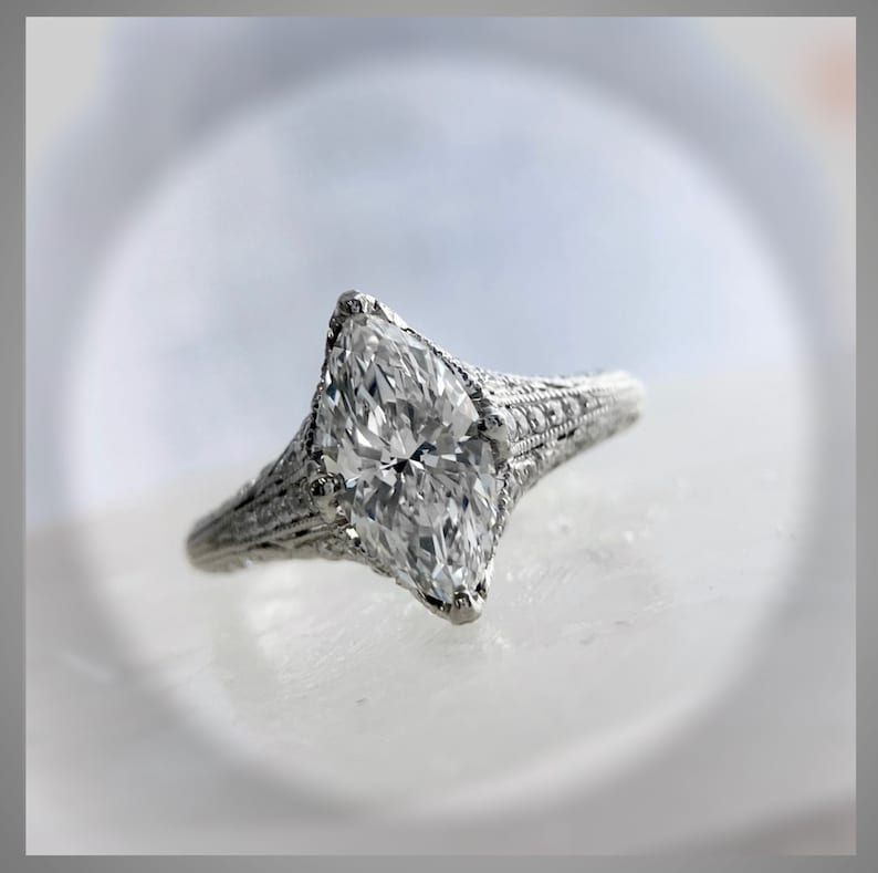 Pu&ograve; includere: Un anello di fidanzamento in argento con un grande diamante chiaro a forma di marquise. La fascia &egrave; decorata con dettagli intricati.