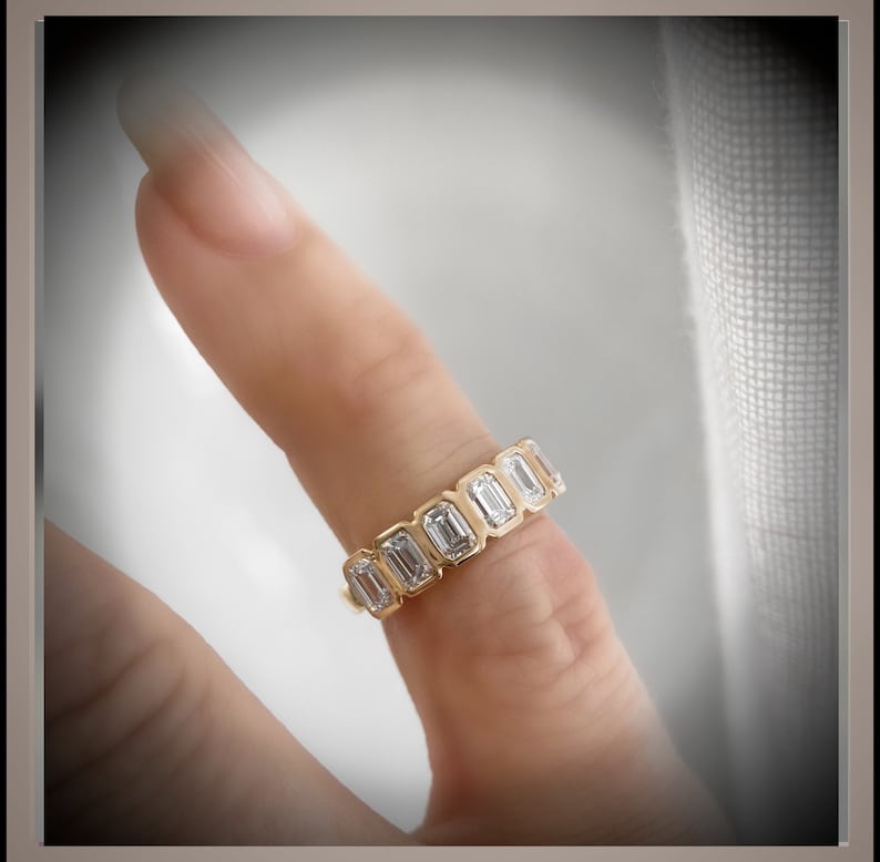 May include: A gold band ring with a row of emerald-cut diamonds.