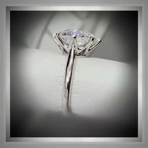 May include: A silver ring with a large, clear, round, prong-set diamond.