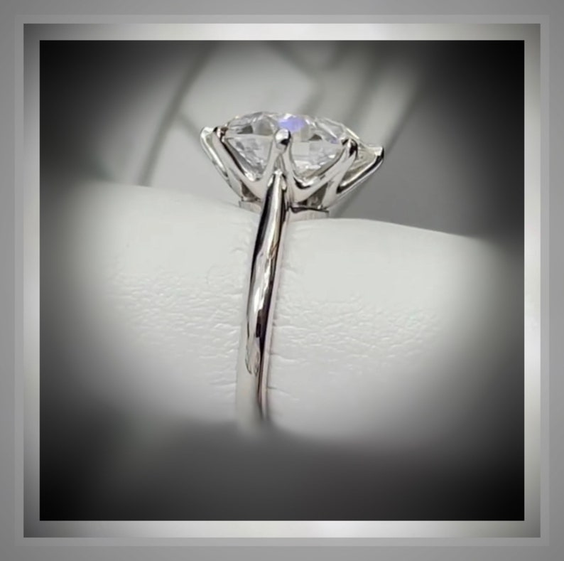 May include: A silver ring with a large, clear, round, prong-set diamond.