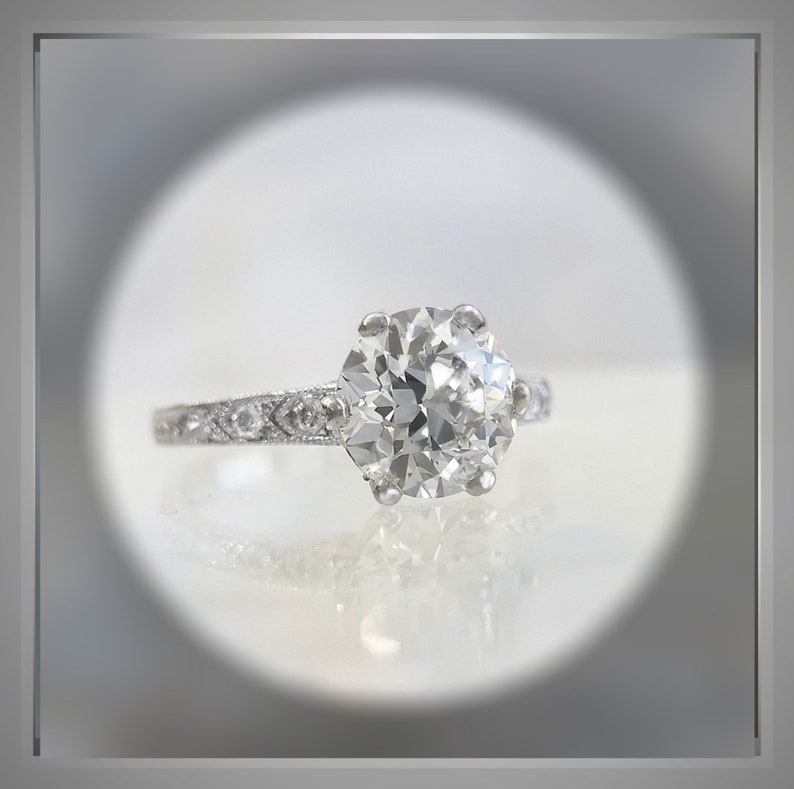 May include: A silver ring with a large, round, clear diamond set in a six-prong setting. The band is decorated with smaller diamonds.