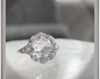 May include: A silver ring with a large, round, clear gemstone surrounded by smaller, clear gemstones. The ring has a delicate, floral design.