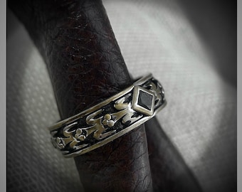 May include: A silver ring with a black gemstone set in a diamond shape. The ring is decorated with intricate floral designs.