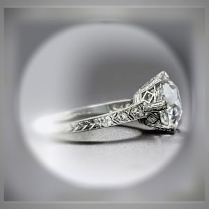 May include: A silver engagement ring with a large, round, clear diamond set in a filigree design. The band is also decorated with smaller diamonds.