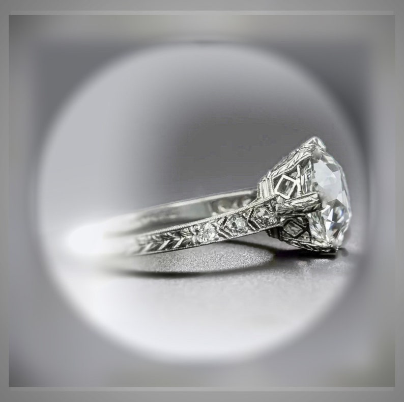 May include: A silver engagement ring with a large, round, clear diamond set in a filigree design. The band is also decorated with smaller diamonds.