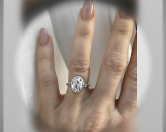 May include: A silver ring with a large, clear oval-shaped gemstone. The ring is on a person's finger.