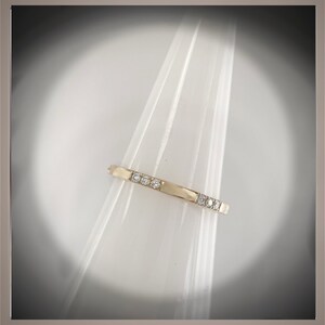 May include: A thin gold band ring with small diamonds set in a row.