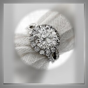 Op de afbeelding: Een close-up van een diamanten verlovingsring met een halo-setting. De ring is gemaakt van witgoud en heeft een grote, ronde middelste steen die omringd is door een cirkel van kleinere diamanten.