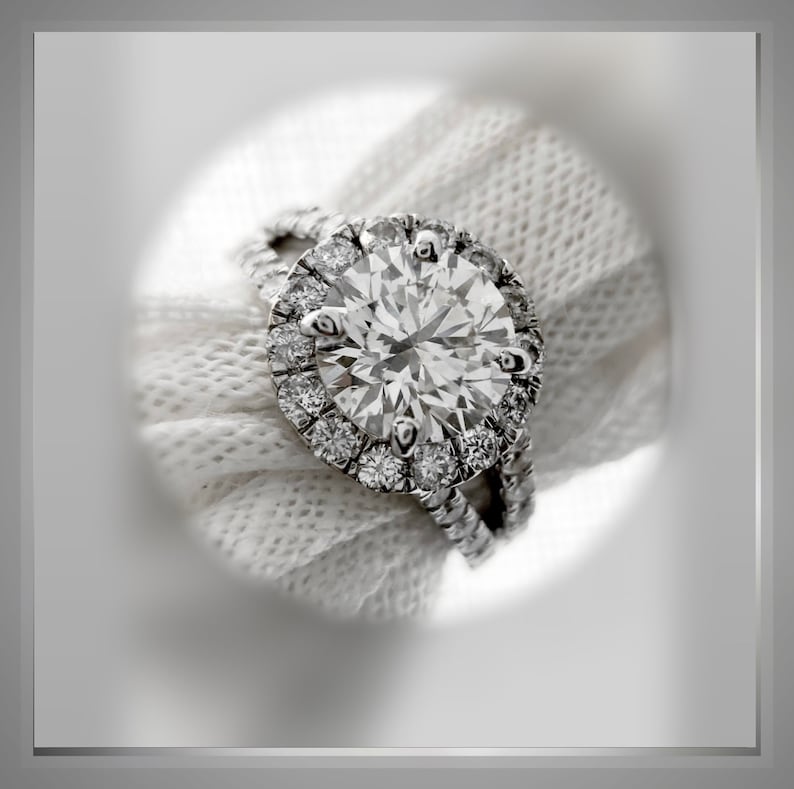 Op de afbeelding: Een close-up van een diamanten verlovingsring met een halo-setting. De ring is gemaakt van witgoud en heeft een grote, ronde middelste steen die omringd is door een cirkel van kleinere diamanten.