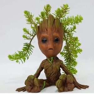 May include: A brown and green ceramic planter shaped like the character Groot from the Guardians of the Galaxy movie. The planter has a small succulent plant growing out of the top.