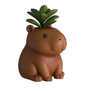 Puede incluir: Una maceta marrón con forma de carpincho con una planta verde que brota de su cabeza. La maceta tiene una superficie lisa, orejas pequeñas y una expresión sonriente. La planta tiene múltiples hojas verdes.