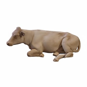 Puede incluir: Figurilla de vaca tallada en beige claro en posición de descanso. La vaca está tumbada con las patas metidas debajo del cuerpo. La figurilla tiene un acabado liso y mate, sobre fondo blanco.