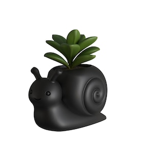 Puede incluir: Una maceta negra con forma de caracol con una planta suculenta verde. La maceta tiene una cara sonriente y un diseño de concha en espiral. La planta es de color verde vibrante, contrastando con la maceta oscura.
