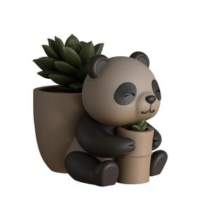Puede incluir: Una maceta con forma de panda con una planta suculenta y una pequeña maceta con forma de bambú. El panda es de color marrón claro con detalles negros y sostiene la maceta pequeña. La maceta más grande es de color marrón claro a juego.