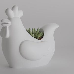 Könnte beinhalten: Ein weißer Keramik-Hühner-Blumentopf mit einer Sukkulentenpflanze im Inneren. Der Pflanztopf hat ein detailliertes Design, einschließlich Kamm, Kehllappen und Flügel. Die Sukkulente hat grüne Blätter. Der Pflanztopf ist ein Dekorationsartikel für die Inneneinrichtung.