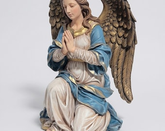 May include: A kneeling angel statue with folded hands, wearing a blue and white robe with gold trim. The angel has brown hair and large, detailed gold wings. The statue is a religious figurine.