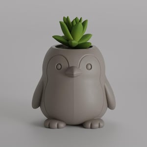 Puede incluir: Una maceta gris con forma de pingüino con una planta suculenta verde. La maceta tiene un acabado liso y presenta un pico, ojos y brazos en forma de aletas. La suculenta es de un verde vibrante, que contrasta con el color neutro de la maceta.