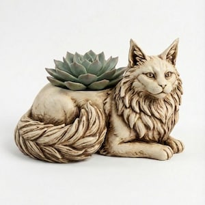May include: A cream-coloured cat-shaped planter with a succulent plant. The cat is sculpted with detailed fur and features, with the succulent nestled in a depression on its back. The planter is made of a durable material and is suitable for indoor or outdoor use.