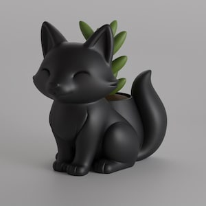 May include: A matte black fox-shaped planter with a small succulent plant. The fox has closed eyes and a smiling expression. The planter is a decorative item for home or office.