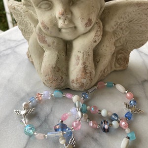May include: Three beaded bracelets with silver angel wing charms. The bracelets are made with light blue, pink, and white beads.