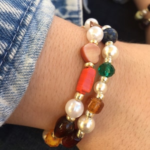 May include: Two bracelets with white pearls, orange, brown, and green beads. One bracelet has a heart-shaped bead and the other has a square bead.