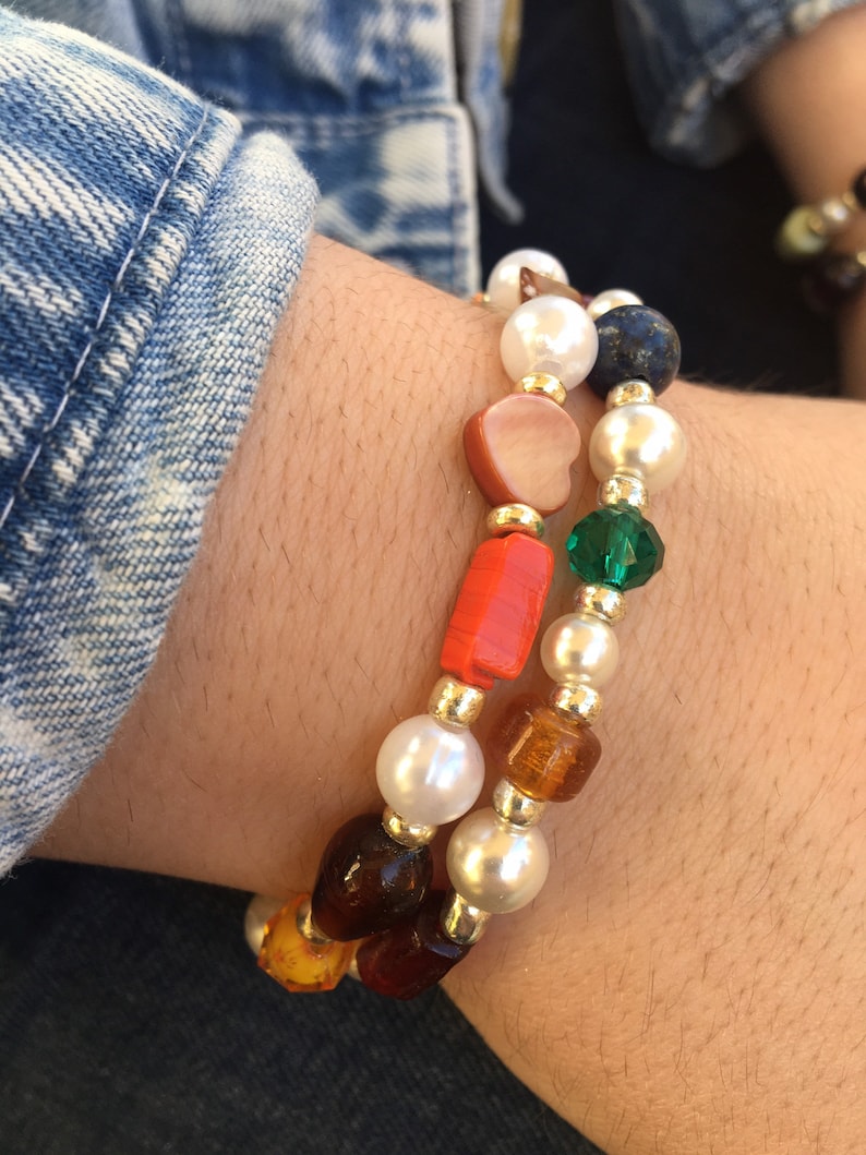 May include: Two bracelets with white pearls, orange, brown, and green beads. One bracelet has a heart-shaped bead and the other has a square bead.